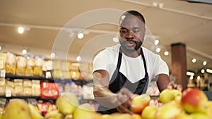 Close-up: A black man in a white T-shirt and black apron arranges yellow pears on a supermarket counter