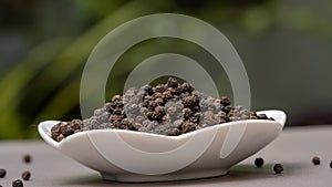 Close up black pepper seeds or peppercorns in white plate outdoor.