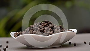 Close up black pepper seeds or peppercorns in white plate outdoor.