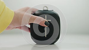 Close-up black portable speaker with female hand pressing plus sign adding volume. Unrecognizable Caucasian young woman