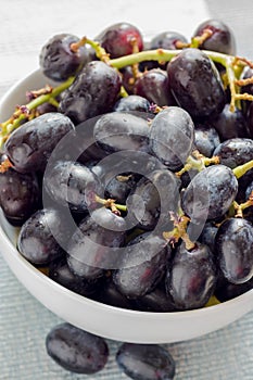 Close up black seedless grapes in a white ceramic bowl