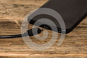 Close-up of black smartphone charging battery with an USB cable on wooden table with copy space