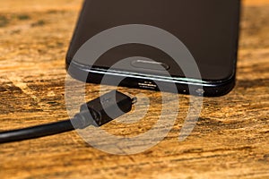 Close-up of black smartphone charging battery with an USB cable on wooden table with copy space