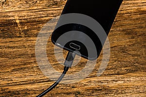 Close-up of black smartphone charging battery with an USB cable on wooden table with copy space