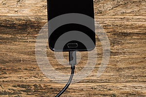 Close-up of black smartphone charging battery with an USB cable on wooden table with copy space