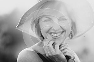 Close-up black and white portrait of a beautiful blonde girl who looks at the camera and smiles joyfully in a hat