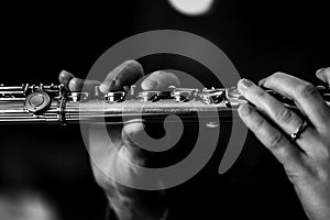 A close up black and white portrait of the fingers of a hand of a flutist musician gripping down on the valves of a silver metal
