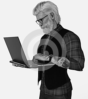 Close-up black and white portrait of a handsome tattooed silver fox with hipster glasses working on a laptop on an isolated white