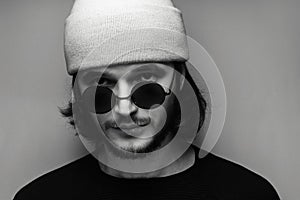 Close-up, black and white portrait of young man wearing sunglasses and hat.