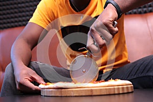 Close-up of a black young man`s hands cutting pizza into pieces. Unrecognizable photo with no face, only hands. Copy