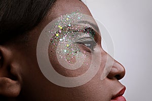 Close-up of black young woman with green mix glitter on her face.  over white background.