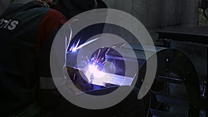 Close-up blacksmith welder in protective mask works with metal using a welding machine, bright sparks. 4K Footage