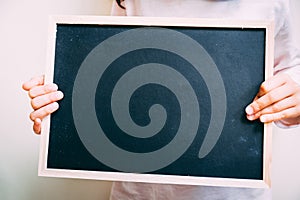 Close up of a blank black chalkboard being held by a child