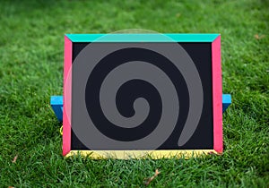 Close-up blank black schoolboard on green grass.Using for insert text. Back to school. Education concept.mockup. Empty chalkboard photo