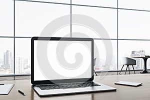 Close up of blank white laptop computer screen on wooden office desktop with supplies on panoramic window and city view background