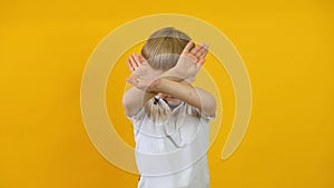 Close up of blond boy crossing arms and showing stop, taboo, prohibition over yellow background