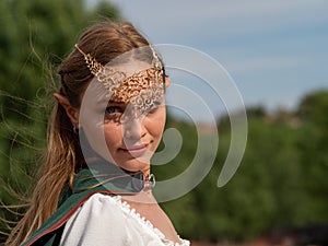 Close-up of blonde girl with blue eyes and elf ears wearing a green cape