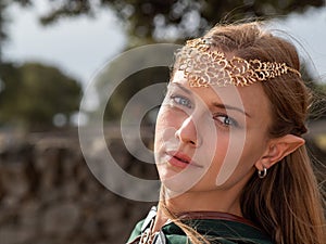 Close-up of blonde girl with blue eyes and elf ears wearing a green cape