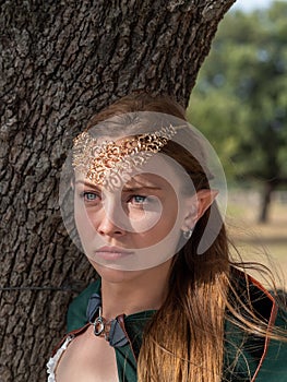 Close-up of blonde girl with blue eyes and elf ears wearing a green cape