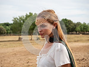 Close-up of blonde girl with blue eyes and elf ears wearing a green cape