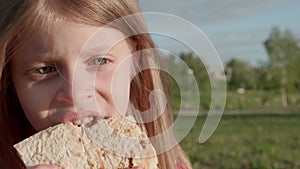 Close-up of blonde hair baby girl chewing shawarma outdoors.