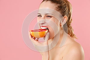 Close up blonde half naked woman 20s perfect skin nude make up blue eyes hold in hand grapefruit isolated on pastel pink