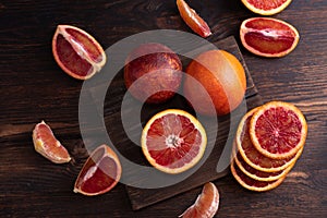 Close up of blood oranges whole, cut into slices and wedges on a dark wooden background, citrus fruit