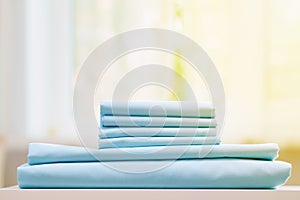 Close-up of blue clean bedding on a blurred background. A stack of folded new bed sheets on the table.