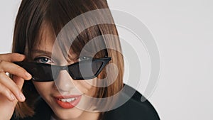 Close up blue eyed girl with bob hair and red lips wearing sunglasses confidently looking in camera isolated on white