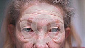 Close up on blue eyes of an elderly woman with wrinkled skin. Depression at old age