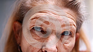 Close up on blue eyes of an elderly woman with wrinkled skin. Depression at old age