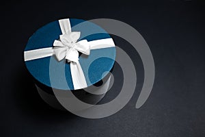 Close-up of blue gift box with white ribbon bow on black background with copy space.