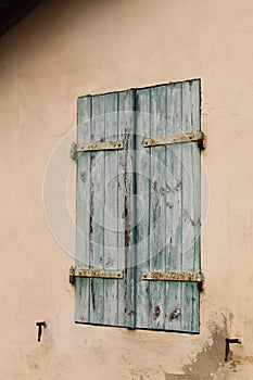 Close up of blue old rustic wooden window shutter closed on beige facade