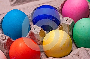 Close-up of blue, pink, red, yellow and green dyed eggs in cardboard egg carton