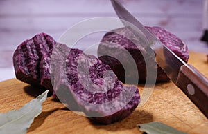 Close-up on blue potatoes, which are cut into wavy circles, near a knife and bay leaves.