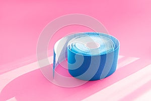 Close up blue roll of kinesiology tape on pink background with trendy sun light and shadows. Recovery, anti-aging procedures