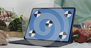 Close-up of blue screen laptop with blurred senior women cooking healthful dietary food in kitchen at home