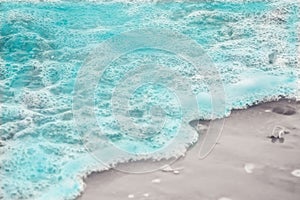 Close up blue sea water waves with white bubbles on sand beach