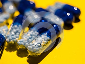 Close up of blue, semi transparent pills with white and pale blue medicine pellets on yellow background