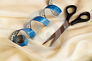 Close up of blue twisted tape measure and black scissors on cream fabric with drapes