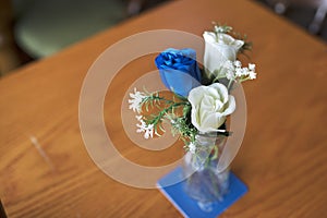 Close up of blue and white artificial roses as a table decoration in a small glass vase at a traditional English wedding in the UK