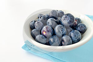 Close-up of Blueberries in White Bowl with Blue Napkin isolated on White