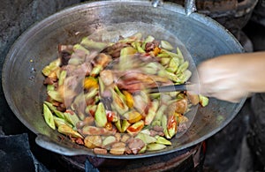 Close-up, blurry motion of a female cook's hand roasting and stir-frying pork