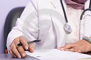 Close up of body part female doctor hand writing prescription recipe on the paper with pen on the table