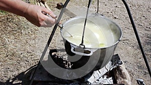 Close-up of boiling fish soup in a saucepan over a fire during a hike, a tourist interferes with the ear with a slotted