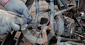 Close-up of a bolt being removed from a broken ATV part. A man holds a screwdriver in his hands and tightens a bolt on