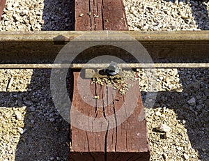 Close up bolted butt of rails and wooden sleepers laid on groundwork crushed stone.
