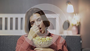 Close up of boring woman sitting on the sofa, eating popcorn and watching TV