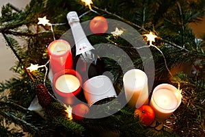 Close up of bottle of champagne with candles and some tangerines in blurred Christmas tree background. Flatlay