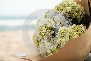 A close-up of a bouquet of blue and yellow hydrangeas that lies on the beach.